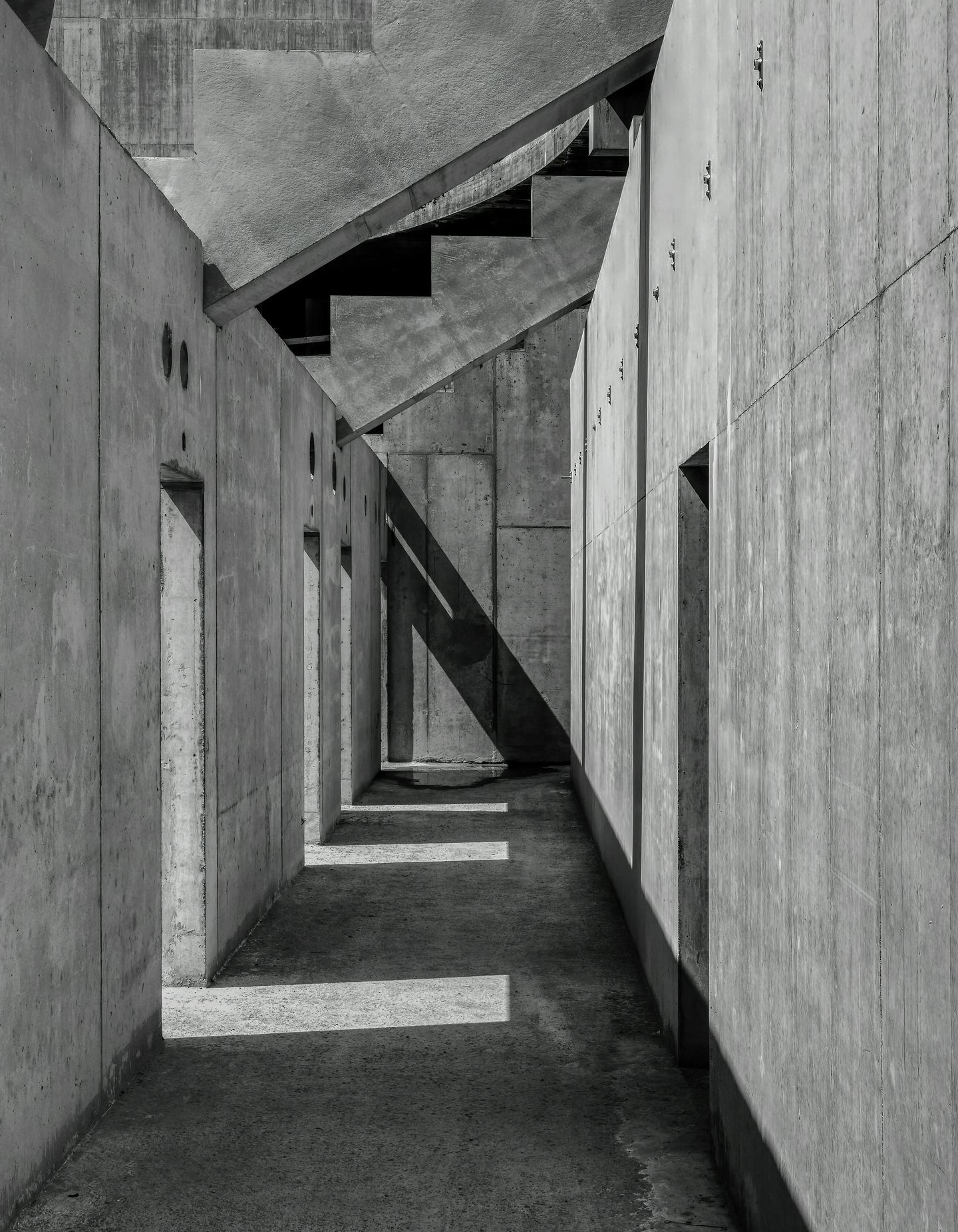 Narrow concrete passage with stairs and stripes of light